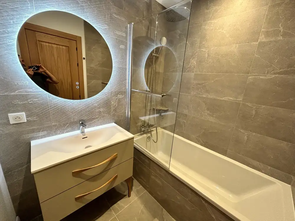 Salle de bains avec baignoire et paroi vitrée, meuble vasque suspendu et miroirs rétroéclairés.