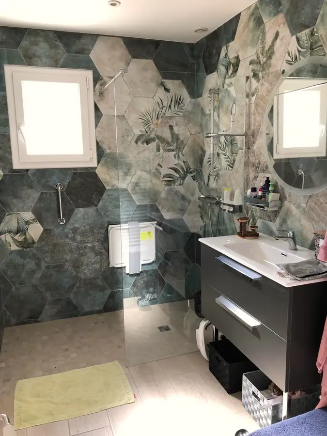 Salle de bains avec carreaux hexagonaux à motif végétal, douche de plain-pied et meuble vasque anthracite.