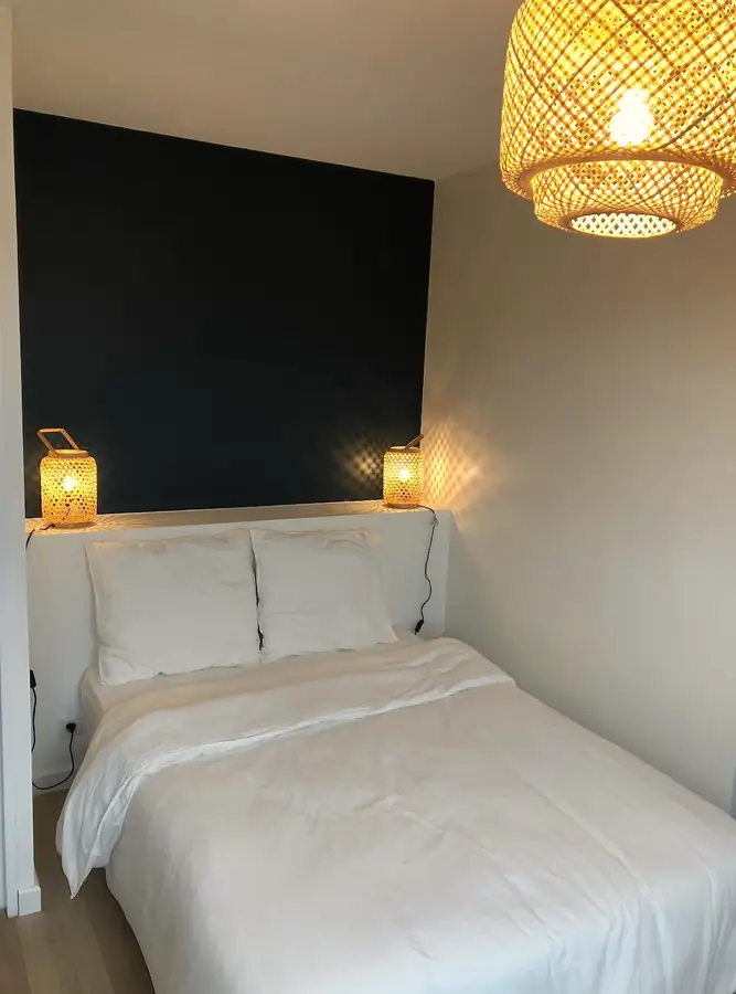 Chambre avec mur vert sombre, lit blanc et suspension en rotin.