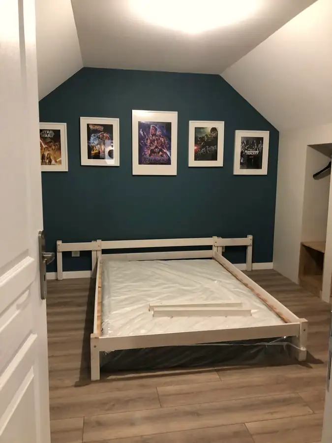 Chambre sous combles avec mur bleu canard et parquet clair.