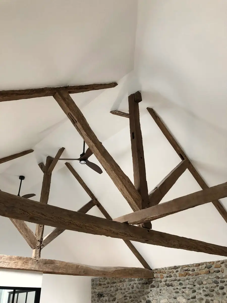 Charpente en bois ancienne conservée et mise à nu, sous un plafond blanc rampant.