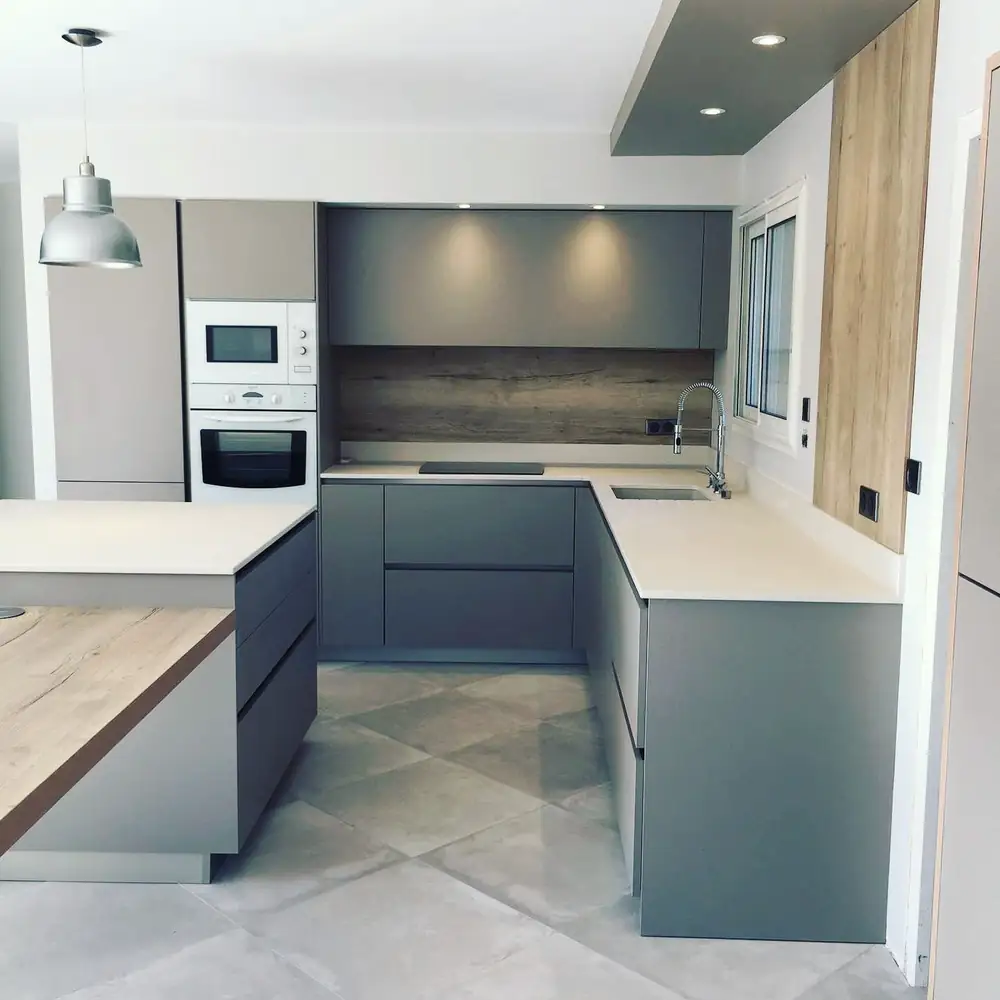 Cuisine grise en L avec colonne four, plan de travail bois et sol en carreaux gris.