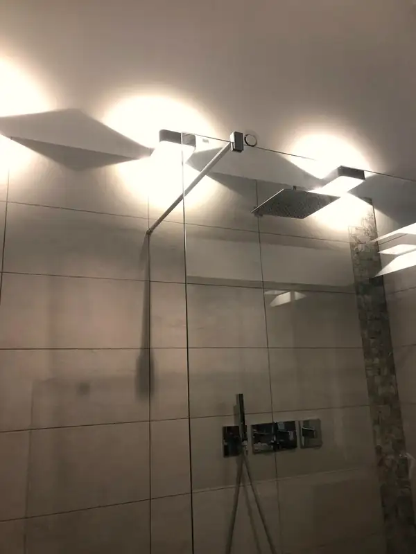 Douche avec pommeau de tête, mitigeur encastré et carrelage grand format.