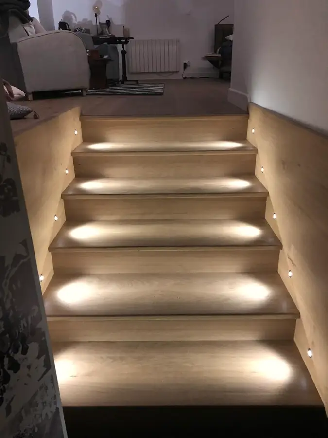 Escalier aux marches en bois éclairées par des spots encastrés dans le mur.