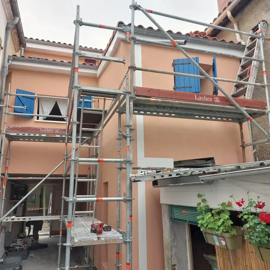 Façade enduite sous échafaudage, volets bleus, pendant les travaux.