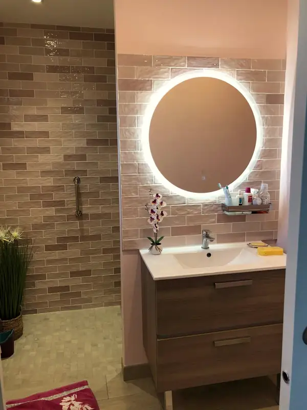 Miroir rond rétroéclairé au-dessus d'un meuble vasque bois, mur en briquettes.