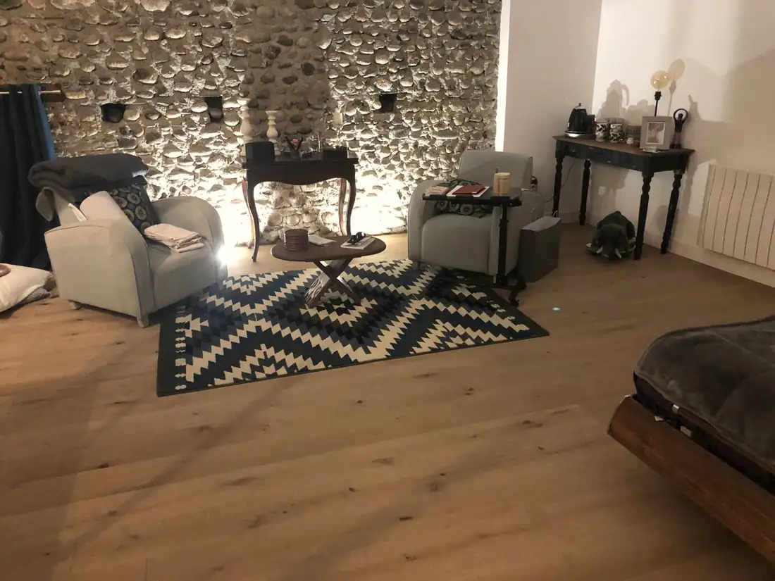 Salon rénové avec mur en galets roulés apparent, poutres et parquet clair.