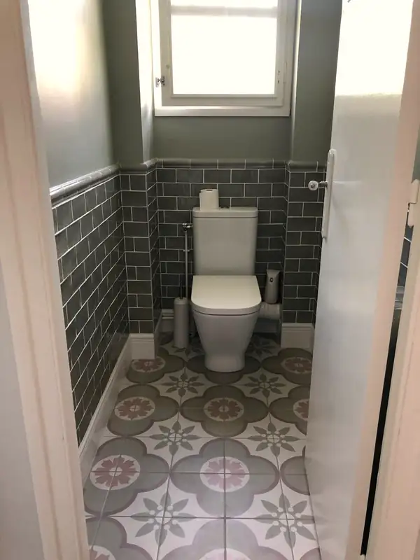 Toilettes avec sol en carreaux de ciment et soubassement en faïence verte.